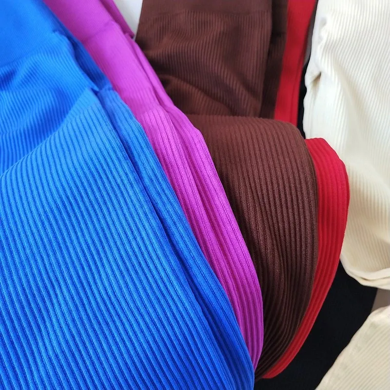 Close-up image of ribbed fabric leggings in multiple colors including blue, purple, brown, red, cream, and black, folded and layered together.